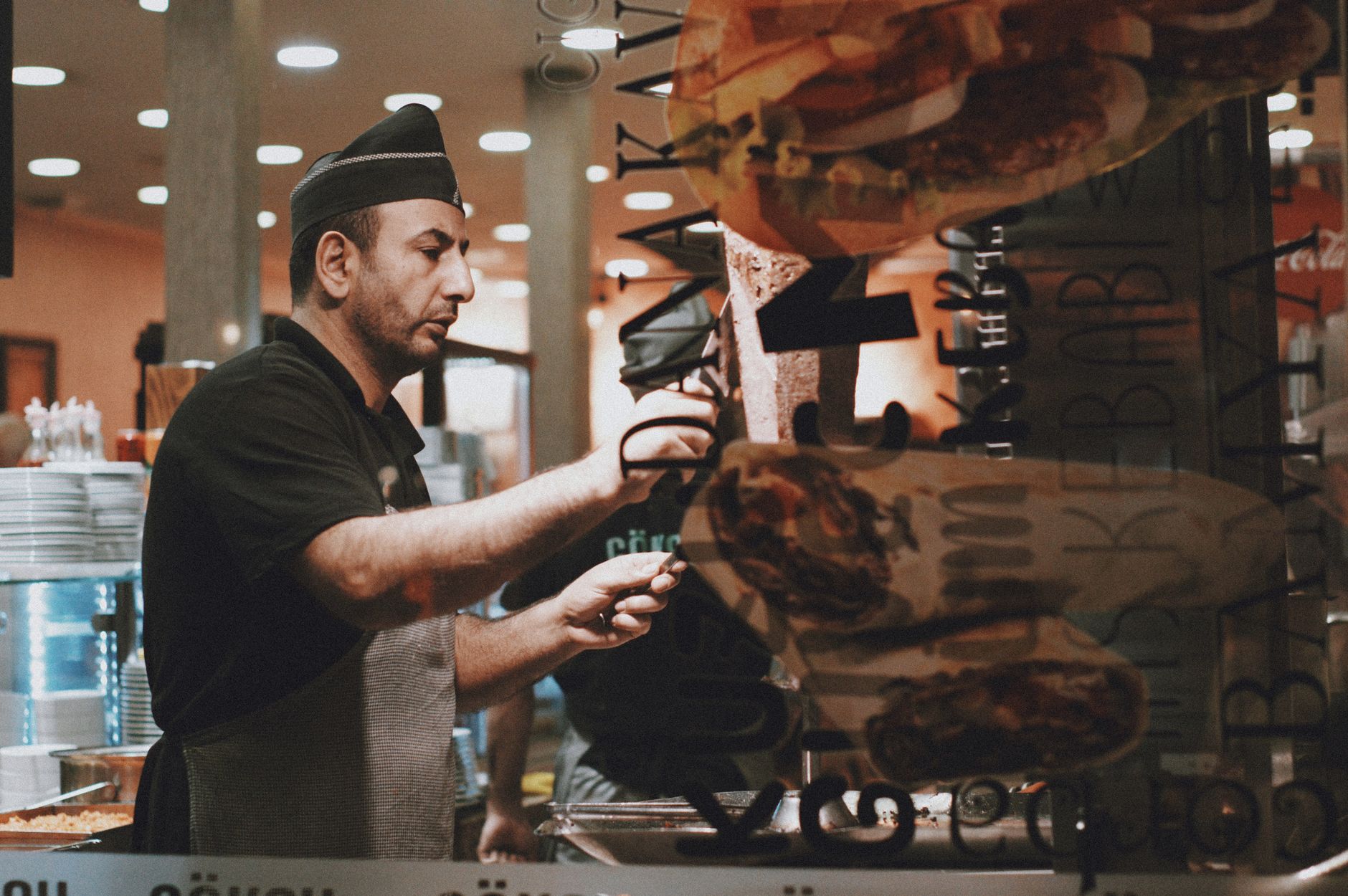 A chef in a black uniform prepares a doner kebab in a restaurant kitchen.