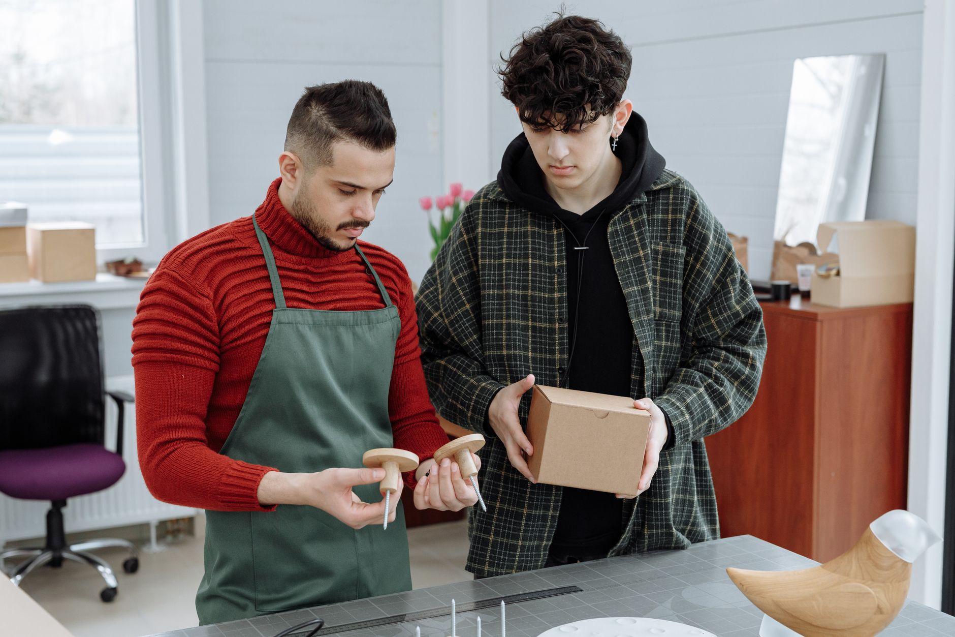 Two men reviewing packaging and craft items in a workshop setting. Collaboration and teamwork.