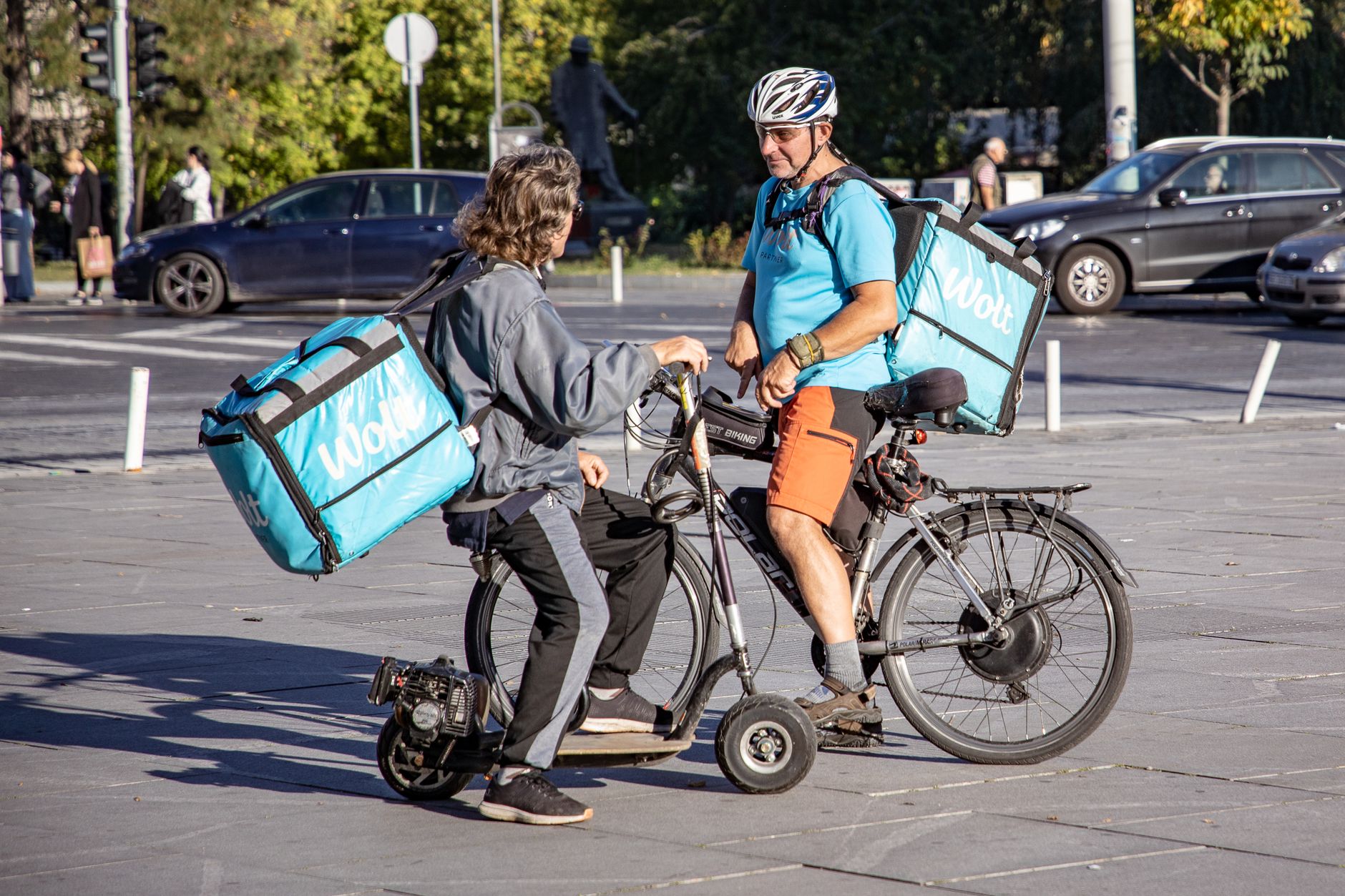Two delivery couriers on bikes having a discussion on a city street.