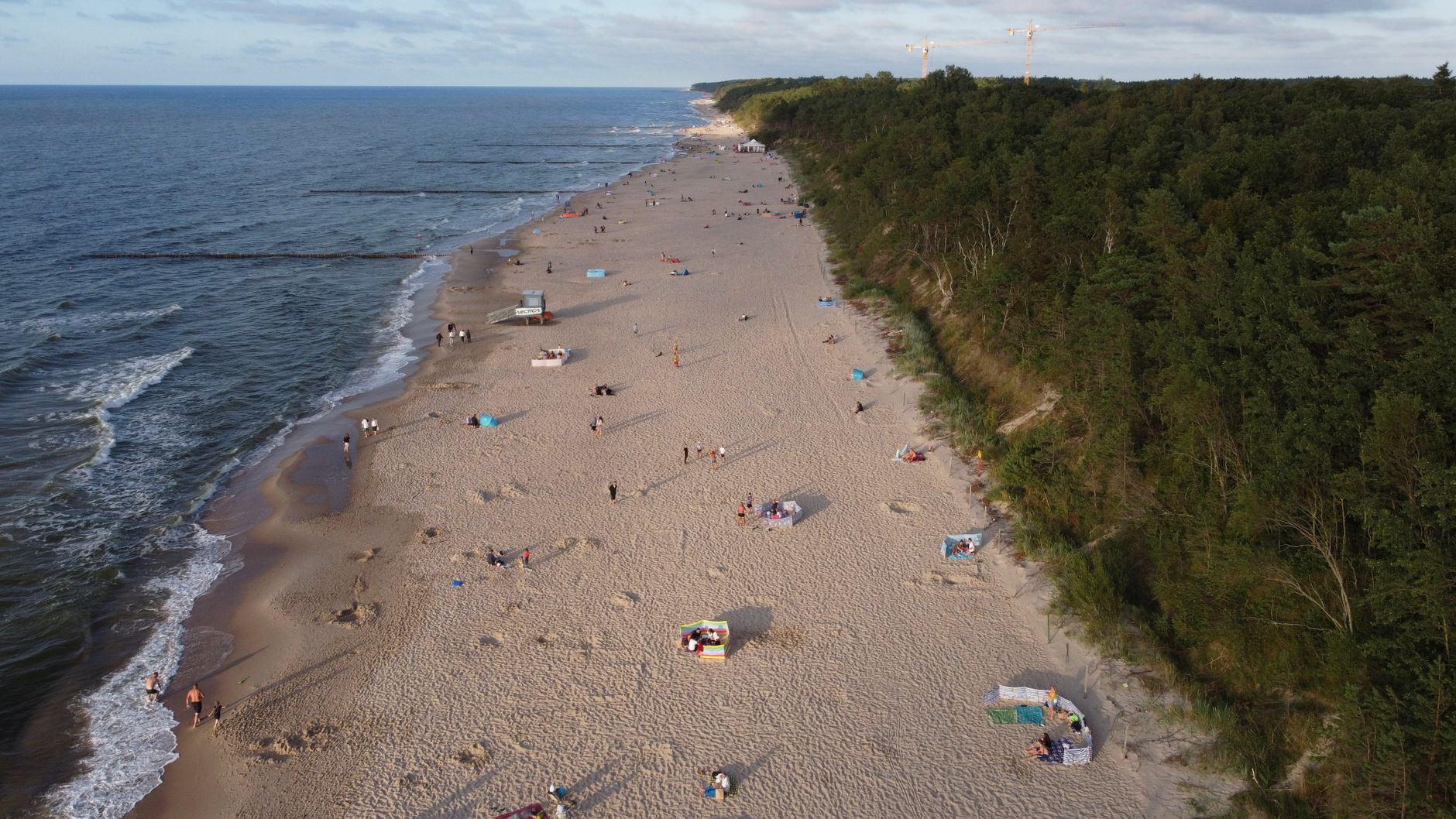 A stunning aerial view of a sandy beach along the Baltic Sea, bordered by lush forests.