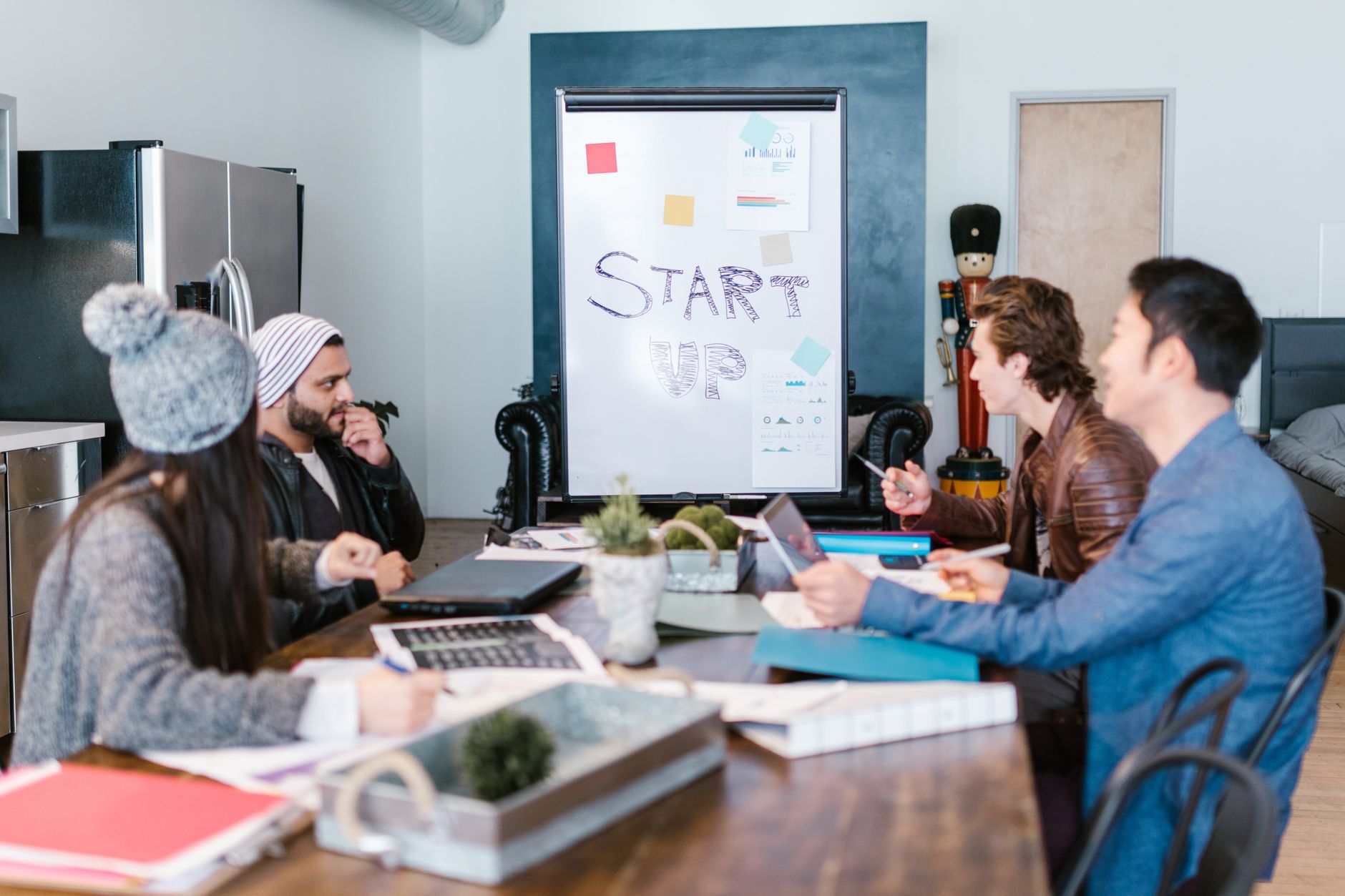 A diverse group of adults working around a table in a startup office, planning and discussing ideas.
