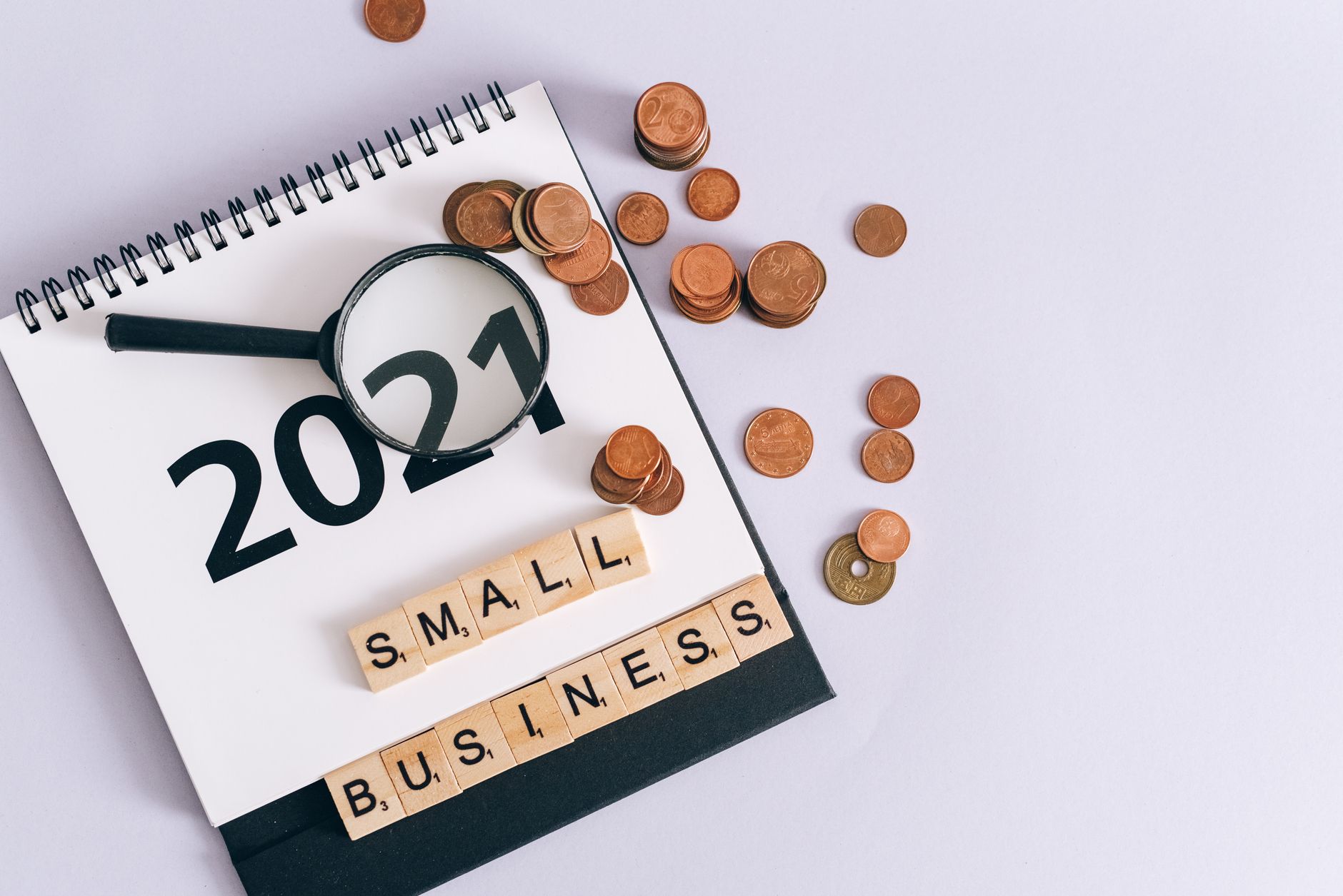 Flat lay of 2021 calendar, coins, magnifying glass, and 'small business' scrabble tiles.