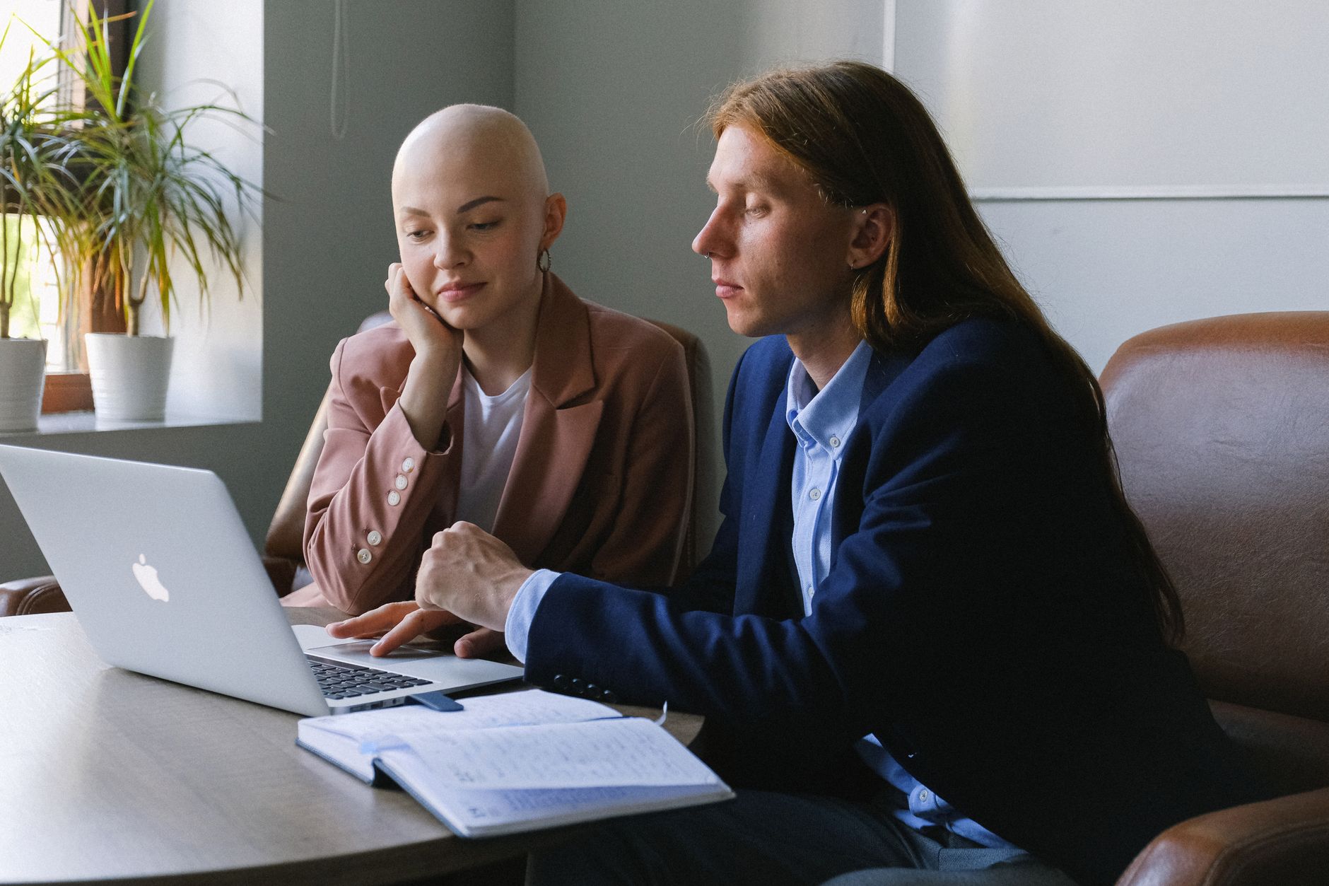 Focused young man and woman wearing formal clothes sitting together at table with laptop and planner while working on new project