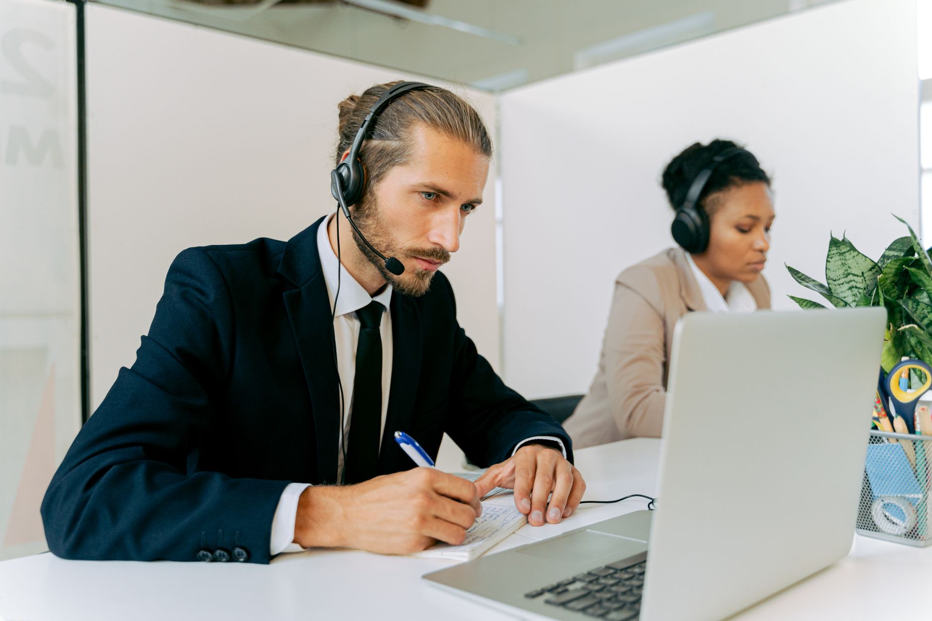 Customer service agents working together at desks, using laptops and headsets.