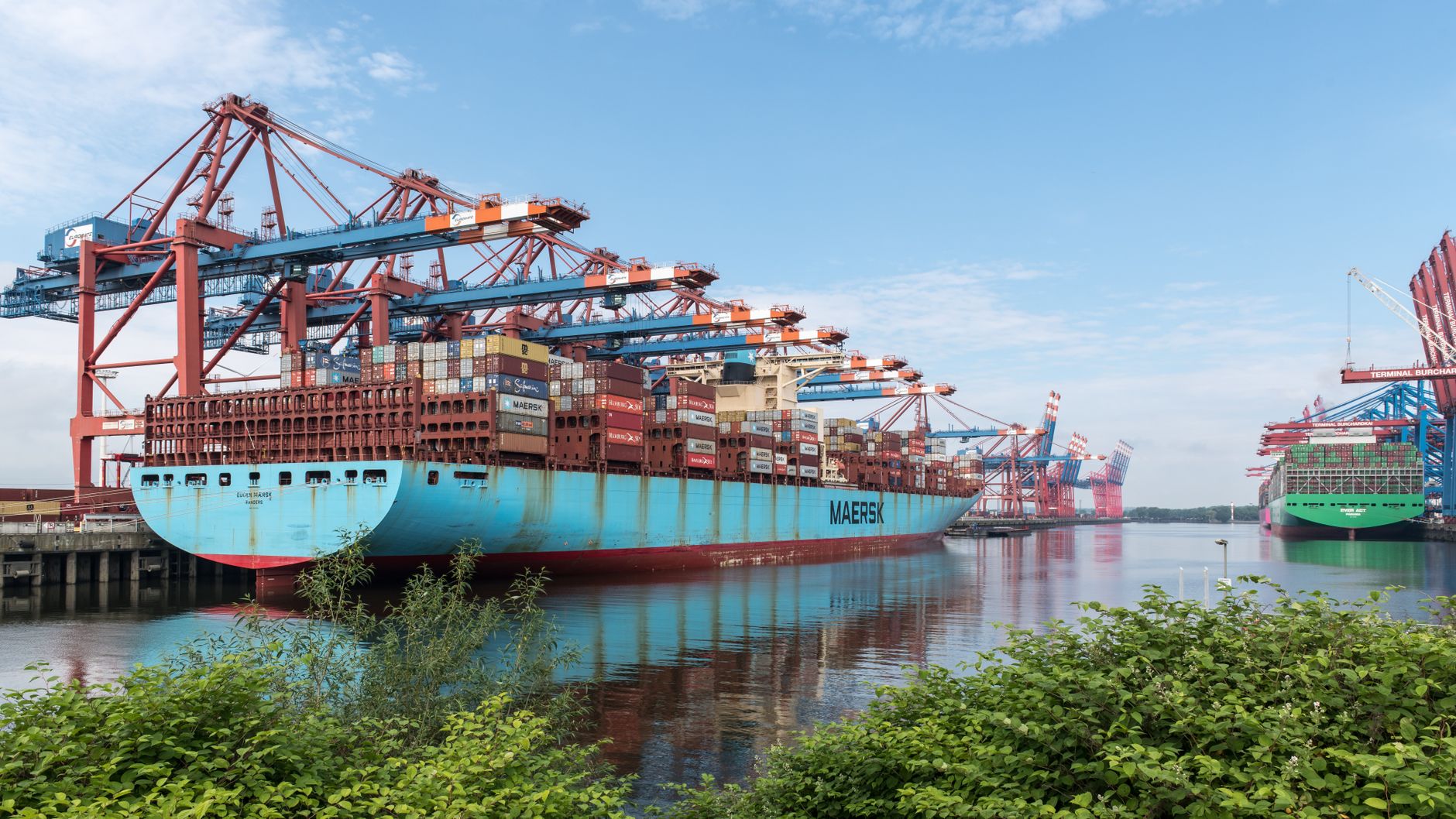 Large container ship docked in Hamburg port, surrounded by cranes and cargo containers.