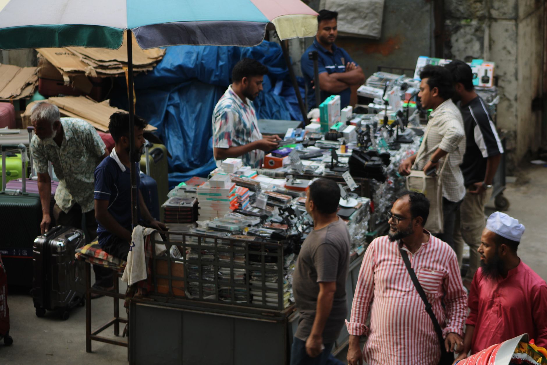 Vibrant market scene with diverse vendors selling electronics under colorful umbrellas.