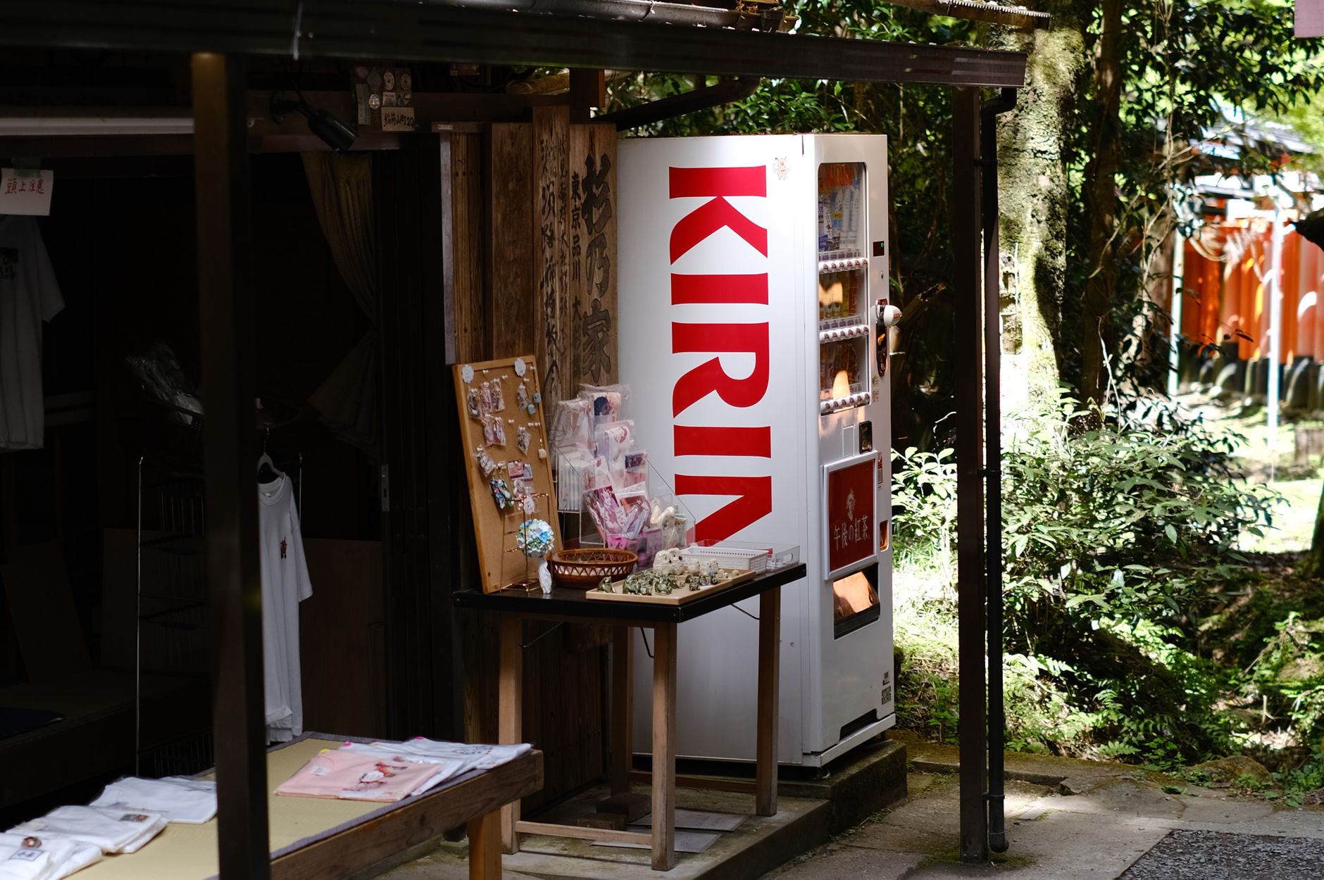 Outdoor vending machine at a Japanese market stall surrounded by greenery, offering snacks and beverages.