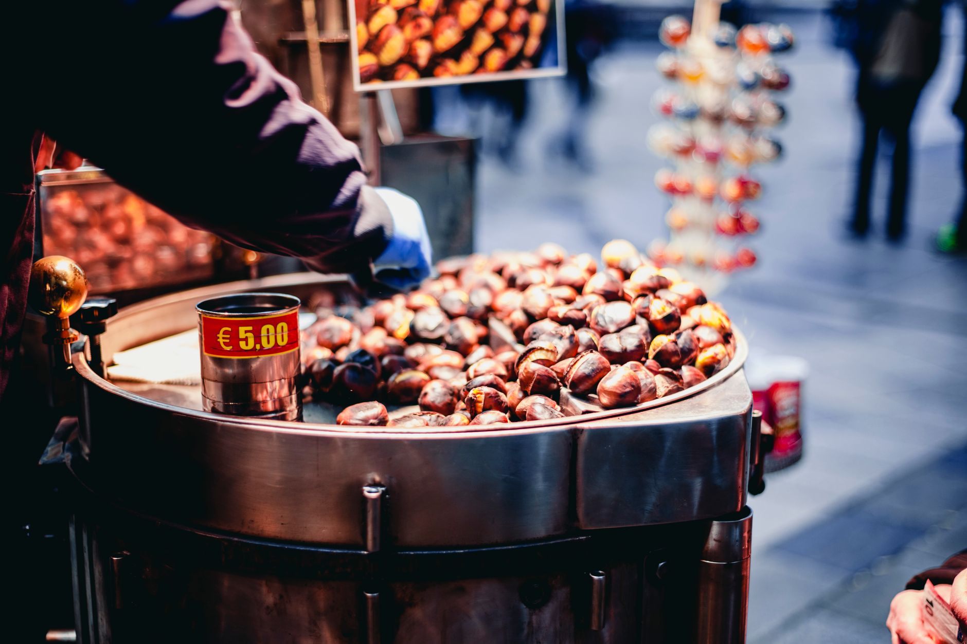 Street vendor selling roasted chestnuts in a market stall with price displayed.