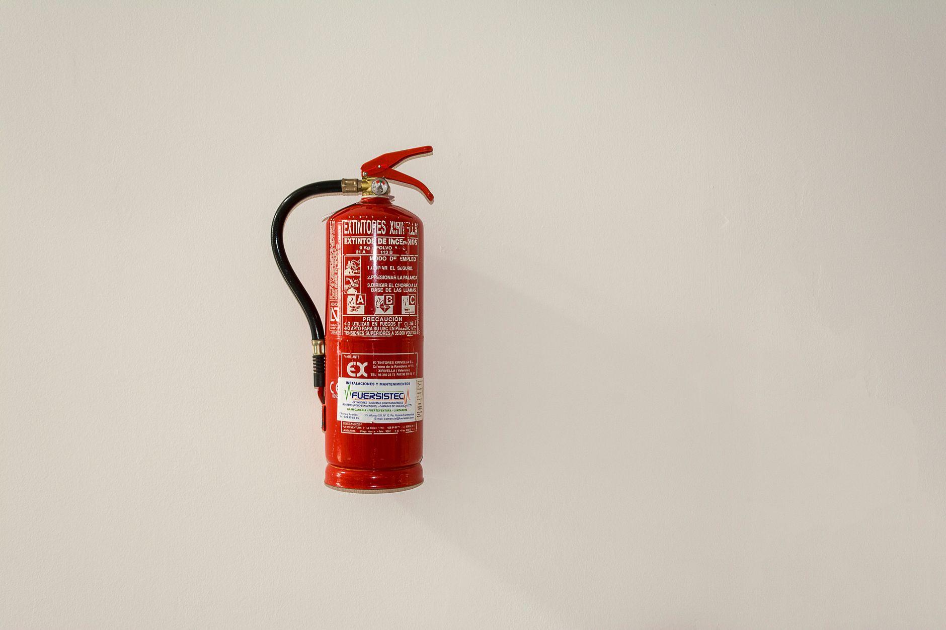 A red fire extinguisher mounted on a plain white wall for emergency safety.