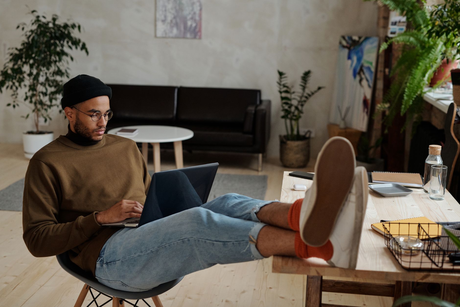 Casually dressed man freelancing with laptop in stylish, plant-filled home office.